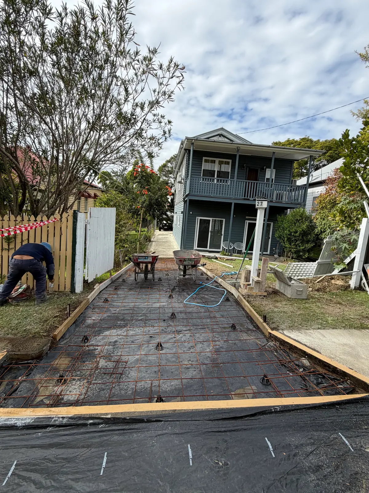 Steel mesh tied over plastic membrane in a formed up driveway, with a worker on the reo