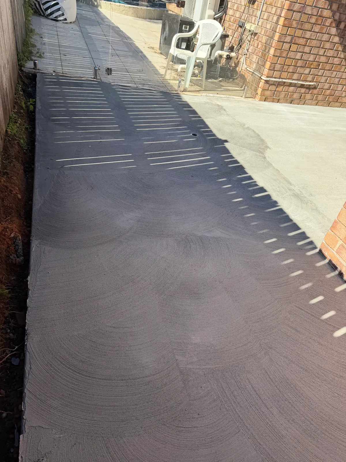 Path freshly poured and finished along a brick wall